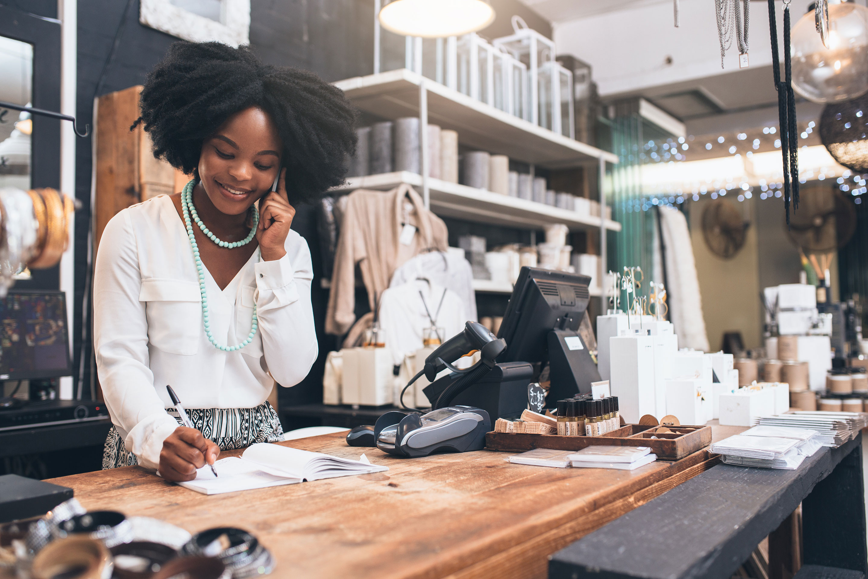 Woman Working in Store on the Phone, Writing Notes While at Front Desk